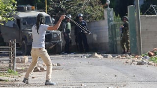 Ein Mann wirft Steine mit einer Steinschleuder gegen uniformierte Sicherheitskräfte