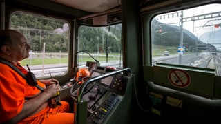 Kowatsch in orangem Überkleid im Lokführerstand mit zwei umgehängten Funkgeräten vor der Einfahrt in den Tunnel.