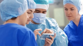 Ein Chirurg und seine Kolleginnen blicken auf ein Smartphone.