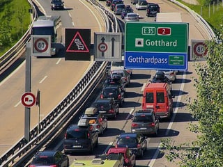 Autokolonne auf der Autobahn, darüber die Verkehrstafel mit der Aufschrift Gotthard