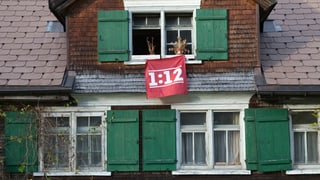Eine Fahne mit der Aufschrift 1:12 hängt an einer Hausfassade.