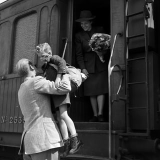 eine schwarz-weiss Fotografie, wie ein Kind von einem Mann aus dem Zug gehoben wird