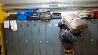 Ein Flüchtling in einer Asylunterkunft hievt einen Koffer von einem Spind herunter. 
