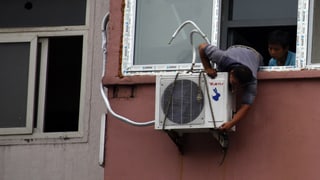 Ein Mann montiert ein Klimagerät unter einem Fenster.