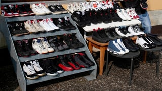 Ein Regal vor einem Haus mit 40 Paar Basketballschuhen drauf, daneben ein junger Mann. Ein Regal vor einem Haus mit 40 Paar Basketballschuhen drauf, daneben ein junger Mann.