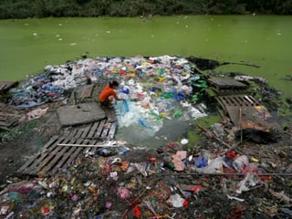 Frau wäscht Wäsche in einem verschmutzten Fluss in Tianjin, China.