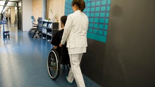 Krankenschwester schiebt Patienten im Rollstuhl durch einen Gang