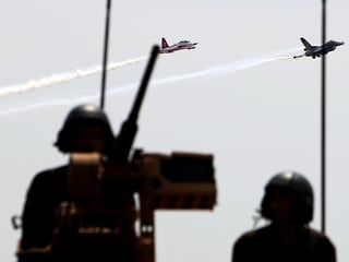 Zwei Kampfjets am Himmel. Im Vordergrund sind zwei Soldaten zu sehen.