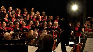 Die Sängerinnen sind schwarz-rot gekleidet und singen im Chor.