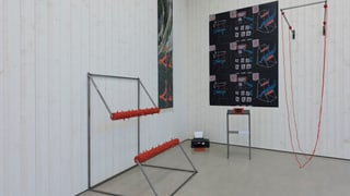 Eine Wand mit zwei dunklen Bildern und zwei metall Gebilden am Boden.