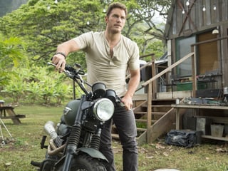 Hauptdarsteller Chris Pratt schiebt sein Motorrad durch die Natur.