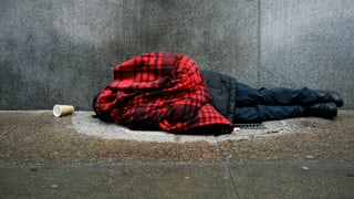 Ein Obdachloser liegt umhüllt in eine Jacke auf dem Boden.