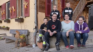 Familie sitzt vor einem Bauernhaus.