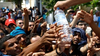 Flüchtlinge strecken ihre Hände nach einer Wasserflasche aus