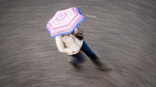 Frau mit Regenschrim geht über die Strasse. 