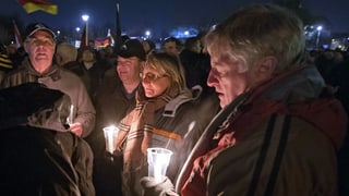 Aufnahme der Demonstranten, mehrere ältere Frauen und Männer stehen herum, sie halten brennende Kerzen.