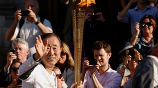 Ban Ki-Moon trägt die olympische Fackel und winkt.