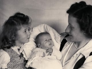 Eine Mutter hält ein Baby auf dem Arm, daneben sitzt ein kleines Mädchen. Eine Mutter hält ein Baby auf dem Arm, daneben sitzt ein kleines Mädchen.
