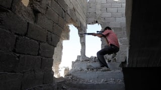 Ein Mann in rot-weiss gestreiftem Shirt schiesst mit einem Gewehr aus einem offensichtlich zerstörten Gebäude heraus auf einen unsichtbaren Gegner.