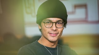 Junger Mann mit Wollmütze und Brille blickt lächelnd in die Kamera Junger Mann mit Wollmütze und Brille blickt lächelnd in die Kamera