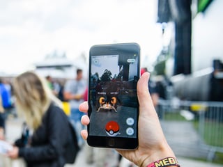Vor Freilichtbühne hält eine Hand hält ein grosses Handy, auf dem ein Pokémon zu sehen ist.