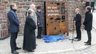 Menschen stehen neben einem Mahnmal Menschen stehen neben einem Mahnmal