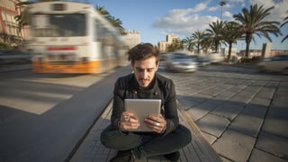 Junger Mann liest auf seinem iPad mitten auf der Strasse.