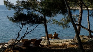 Strand mit Pinien. Liegestühle. In einem sitzt ein Mädchen.