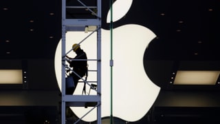 Ein Bauarbeiter auf einem Kran vor einem grossen Apple-Signet.