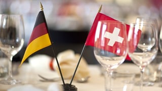 Eine deutsche und eine Schweizer Flagge stehen auf einem Tisch Eine deutsche und eine Schweizer Flagge stehen auf einem Tisch
