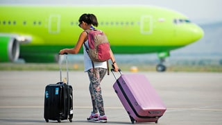 Frau mit Koffer vor einem Flugzeug
