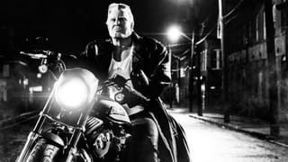 Ein grosser, grimmiger und muskulöser Mann sitzt auf einem Motorrad.