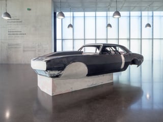 Ein schwarzes Auto steht unter vielen Lampen im Museum.