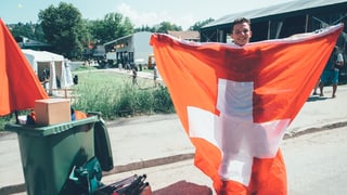 Mann hisst Schweizer Flagge und hat grüne Tonne dabei. Mann hisst Schweizer Flagge und hat grüne Tonne dabei.