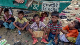 Rohingya-Kinder sitzen in einem Flüchtlingslager in Bangladesh unter einem Transporter für Hilfsgüter.