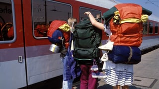 Drei Jugendliche von hinten Fotografiert mit Tramperrucksächen vor einem Zug.