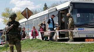 Personen steigen in einen Bus. Im Vordergrund bewacht ein Soldat diese Aktion.