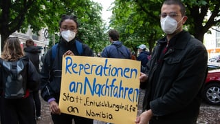 Junge Fraue und junger Mann mit Schild. Aufschrift: Reparation statt Entwicklungshilfe Junge Fraue und junger Mann mit Schild. Aufschrift: Reparation statt Entwicklungshilfe