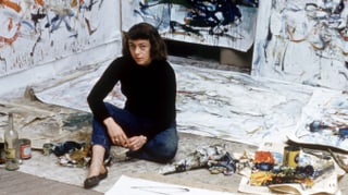 Joan Mitchell, inmitten ihrer Gemälde am Boden sitzend.