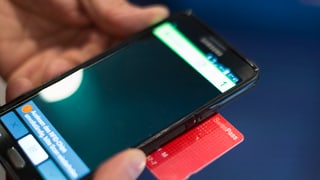 Handy und Swisspass, die ein Kontrolleur im Zug ansieht. man sieht nur Handy, Swisspass und Hände.