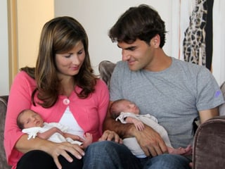 Charlene Riva und Myla Rose als Säuglinge in den Armen von Mirka und Roger Federer, die auf einem Sofa sitzen.