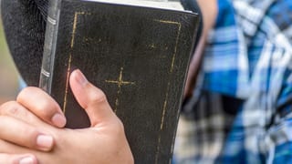 Ein Mann, der seinen Kopf nach unten hält, hat seine Hände auf einer schwarze Bibel.