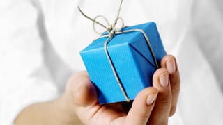 Jemand hält ein kleines, blaues Geschenk in der Hand.