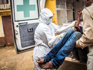 Eine Sanitäterin im Schutzanzug und ein Mann heben einen Patienten mit Ebola-Verdacht in eine Ambulanz in Sierra Leone.