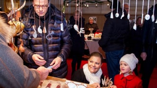 Daniel, Victoria und Estelle von Schweden stehen vor einem Weihnachtsstand.