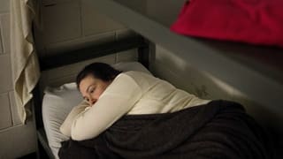 Eine nachdenkliche Frau im Bett ihrer Zelle.