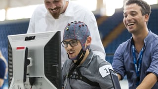 Ein Mann mit einer Elektrodenhaube auf dem Kopf sitzt vor einem Computerbildschirm Ein Mann mit einer Elektrodenhaube auf dem Kopf sitzt vor einem Computerbildschirm