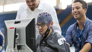 Ein Mann mit einer Elektrodenhaube auf dem Kopf sitzt vor einem Computerbildschirm