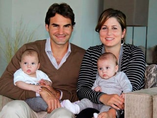 Mirka und Roger Federer mit Myla und Charlene im Arm auf einem Sofa sitzend.