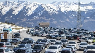 Zahlreiche Autos sind parkiert, im Hintergrund sieht man schneebedeckte Alpen.